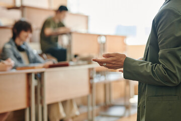 Hand of young confident female teacher in dark green jacket making report describing main points of seminar or lecture to students