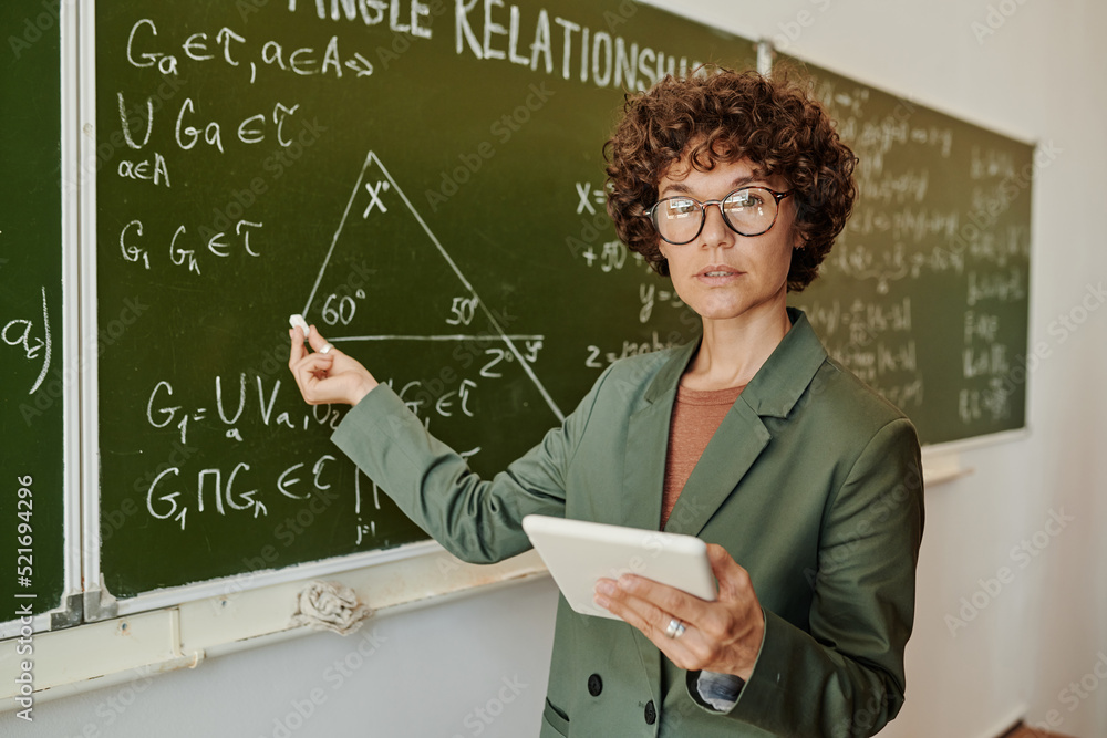 Poster confident teacher of geometry pointing at triangle on blackboard drawn among formulas and equations 