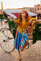 A beautiful girl stands near the carriage on the Djemaa El Fna Square. Morocco Marrakesh