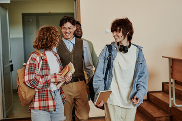 Fototapeta premium Happy highschool teenage students in casualwear discussing news while entering lecture hall in the morning or after break