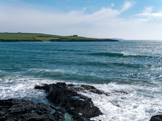 A sea bay on the south coast of Ireland near Clonakilty on a sunny day. Waves and coastal rocks under a clear blue sky. The beauty of Irish nature. Turquoise sea water, rock formation on sea