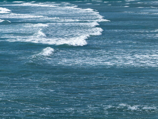 Beautiful white foam on turquoise tidal waves. The surface of the water as a background. Blue ocean water