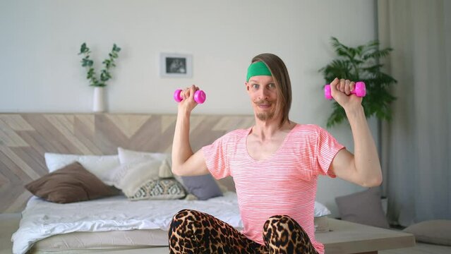 Funny cheerful sportsman crazy fitness man in retro sportswear doing exercise in living-room sport workout home. Crazy sports trainer holding dumbbell, looking at camera. Fitness motivation caricature