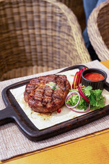 Grilled pork steak on the bone with seasonings and grilled tomatoes on a black background. Top view