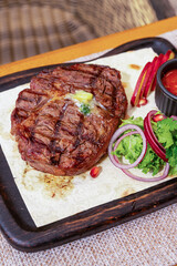 Grilled pork steak on the bone with seasonings and grilled tomatoes on a black background. Top view