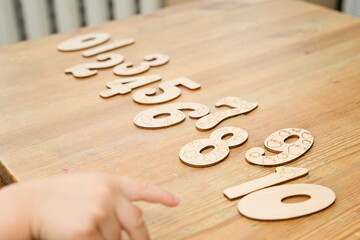 Wooden jigsaw digits from 0 to 10 on natural wood table. Learning numbers. Toy for preschool Kids. Boy pointing number six. Implement for nursery or kindergarten.