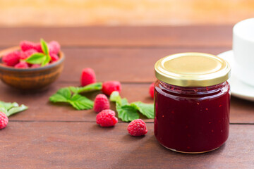 fresh raspberry jam in a glass jar on a wooden table, next to fresh raspberries. concept of homemade jam, preserves for winter, selective focus