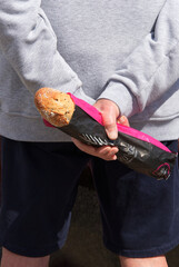 Mann hält mit beiden Händen hinter dem Rücken ein gekauftes Baguette, vertikal