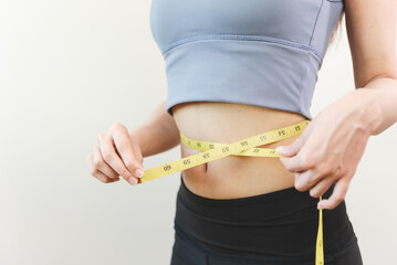 Young slim woman measuring her waist by measure tape after a diet