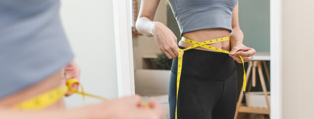 Young slim woman measuring her waist by measure tape after a diet - obrazy, fototapety, plakaty