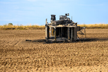 Top view of a burnt out hay baler on its side in a field with debris around it