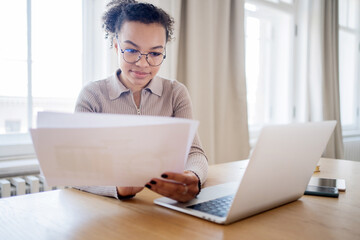 A female freelancer with glasses works in an office, uses a laptop, checks a report in a finance company