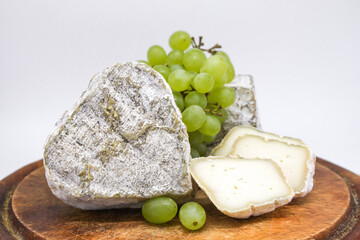 Assorted mouldy blue cheeses goat's milk on a wooden chopping board with green grapes. White background
