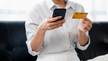 A woman playing smartphone on the sofa in her home living room, she is relaxing on weekends after a hard day's work, she is shopping online and paying by credit card. Credit card payment concept.