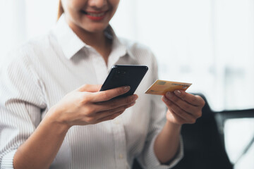 A woman playing smartphone on the sofa in her home living room, she is relaxing on weekends after a hard day's work, she is shopping online and paying by credit card. Credit card payment concept.
