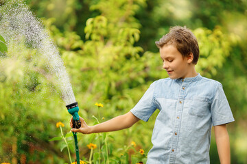Boy watering flower in garden. Kid with pours water from a hose on summer day. 