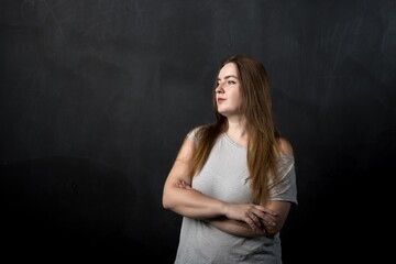 a girl of European appearance with folded hands looks to the side against the background of a black slate wall. vertical photo, place for text. Thoughtful teacher or businesswoman