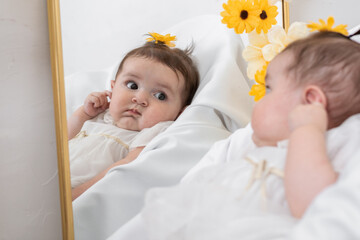 close-up of a beautiful latina baby girl, looking at her reflection in the mirror for the first...