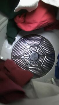 Slow motion vertical video of clothes tumbling in laundry dryer.