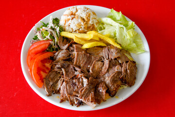 Turkish and Arabic Traditional Ramadan doner kebab with tasty tomato sauce and rice or turkish pilav in white plate on wood table background. ( , Iskender, ekmek arasi pilav ustu doner, doner durum )