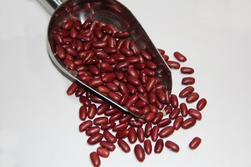 Beans in a stainless steel measuring spoon on a white background, top view.