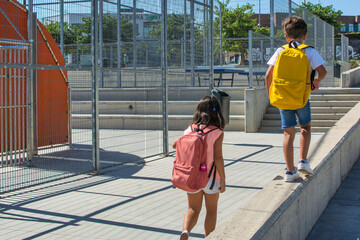 Rear view of Elementary age children walking to school. Boy and girl with backpacks back to school. Classmates. Children playing