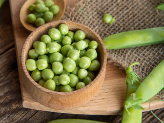 wooden bowl and spoon with fresh peas and their pods on an old wooden table, rustic background with peas