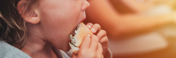 little candid kid boy five year old eats burger or sandwich food sitting in airplane seat on traveling from airport. children take a bite. child in air plane eating lunch or dinner meal. banner. flare