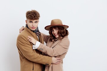a cute couple stands on a light background dressed in coats and sweaters, a man stands against a woman and gently hug each other
