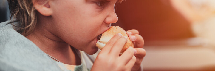 little candid kid boy five year old eats burger or sandwich food sitting in airplane seat on traveling from airport. children take a bite. child in air plane eating lunch or dinner meal. banner. flare
