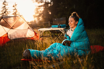 Woman relaxing and lie in a sleeping bag in the tent. Sunset camping in forest. Mountains landscape...
