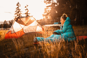 Woman relaxing and lie in a sleeping bag in the tent. Sunset camping in forest. Mountains landscape...