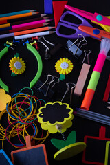 Top view on various bright study equipment lay on black background. Marker, pencil, small chalkboard, scissors, paperclip, chalk. Vertical photo