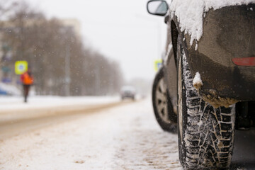 Rear view of a snow-covered car with studded tires on the background of the road and passing cars. The roads are covered with snow. Safety first