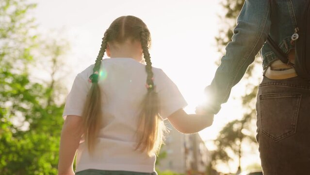 mother leads small child by hand glare sun through park. kid girl sunset walks by hand holding her mother. chidhood dream. happy family. baby walk concept. hand hand sunset. children life. parent kid