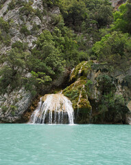 Wasserfall an einer Steilwand stürzt fächerförmig direkt in den türkisen Fluss. 