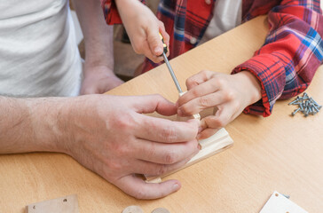 Happy father's day and childhood concept. Close-up of a father and a boy son in glasses work with hand tools, using a screwdriver, assembling a wooden house constructor at the table.