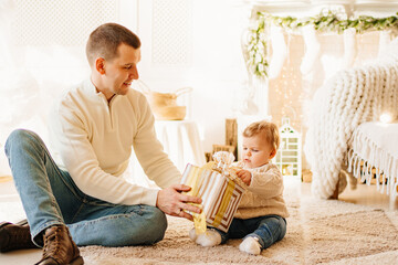 dad give a gift in a box to their young son on the floor of the room. 