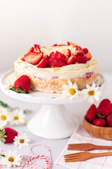 Strawberry vanilla cake on a white cake stand, whith wooden forks and strawberries and white daisies on a white background