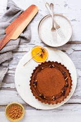 Fototapeta na wymiar Chocolate caramel tart with dry orange sliceon a white ceramic with fork on a wooden surface
