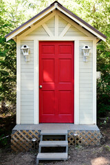 An image of an outdoor composting toilet with a bright red door and solar powered lights. 
