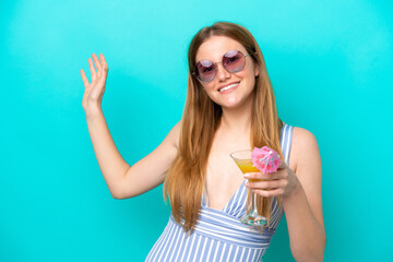 Young woman isolated on blue background in swimsuit and holding a cocktail