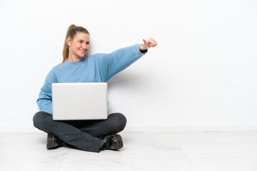 Young woman with a laptop sitting on the floor giving a thumbs up gesture