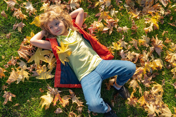 Kids play in autumn park. Children portrait with yellow leaves. Child boy with oak and maple leaf outdoor. Fall foliage. Kid boy lying on ground or grass and fallen leaves in autumn park.
