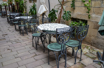 Fototapeta na wymiar Vintage empty round tables and chairs on summer cafe terrace in the old city street 