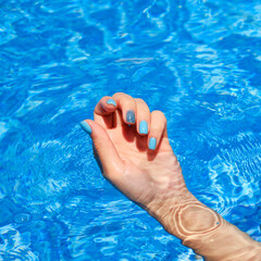 Close-up of female manicured hands. Woman's hands with bright glitter blue fingernails inside of bright blue swimming pool water.