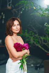 an attractive woman with bare shoulders and arms with a peonies.