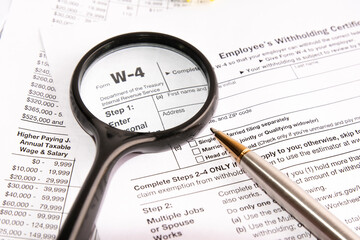 blank form W-4, magnifier and a pen on table. tax season