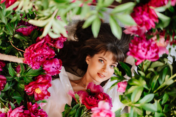 a beautiful and gentle young woman lies in peony flowers. feminine beauty. 