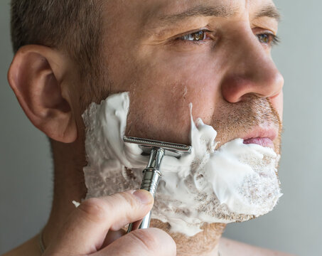 Close-up Of A Man With Long Stubble Shaving With An Old-fashioned T-shaped Chrome Razor